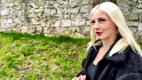 Blonde MILF in fur coat teases with big tits smiling outdoors by stone wall