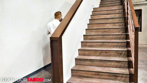 Blonde guy in tight white shirt leans on wooden stairs teasing taboo stepbrother vibe