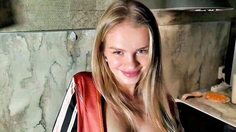 Blonde vixen smirks seductively with deep cleavage spilling from open satin jacket