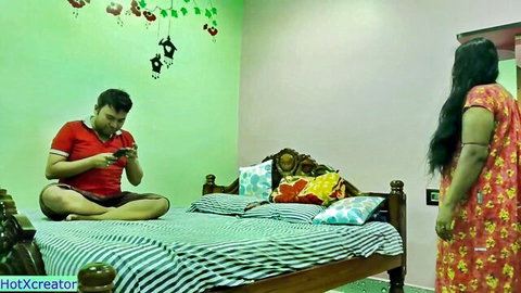 Desi bhabhi in red nighty standing, man on bed watching phone, amateur Indian couple tease