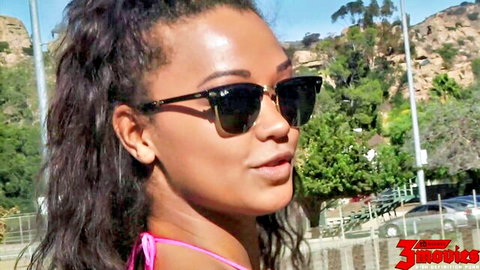 Mixed-race beauty in pink bikini top and sunglasses poses outdoors