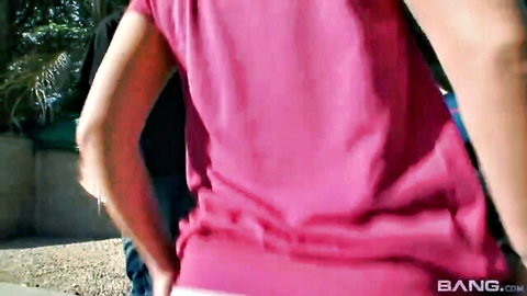 Justina in pink tank top bending over outdoors with man behind