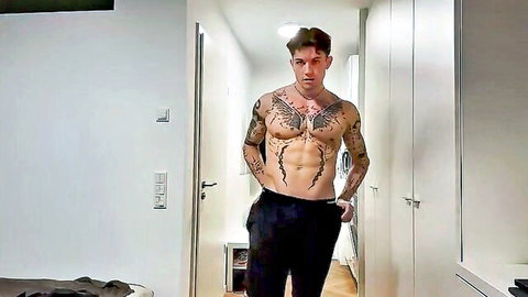 Tattooed muscular guy teases strip in hallway, shirtless and seductive