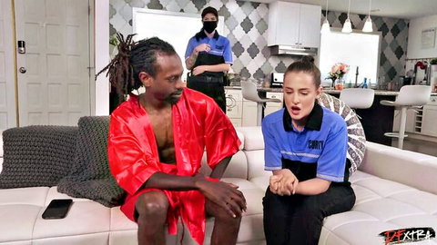 Nikki Zee in security uniform sits with black stud in red robe, teasing interracial encounter