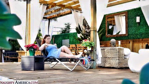 Curvy redhead with huge tits lounging seductively in sheer blue dress on outdoor patio chaise