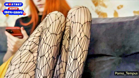 Redhead woman in yellow mini dress and fishnet stockings, legs spread teasingly
