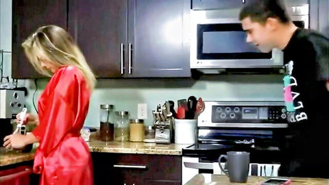 Blonde stepmom in silky red robe at kitchen sink with stepson behind her