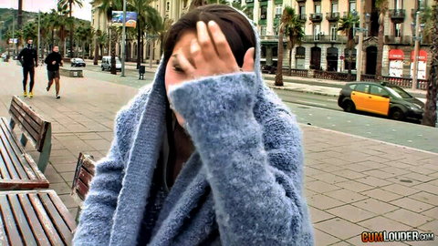 Shy brunette in fuzzy blue coat covering face on public Barcelona bench teasing