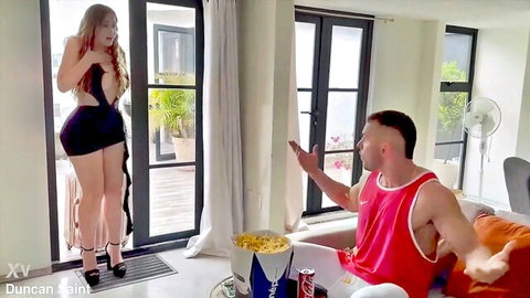 Sexy redhead in skimpy black dress teases muscular guy on couch with popcorn and beer