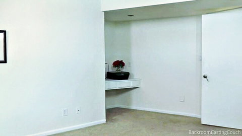 Empty backroom casting couch bedroom with white walls, red flowers vase and open door setup