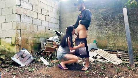 Asian woman kneeling for outdoor blowjob on shirtless man at farm party