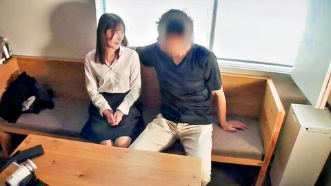 Japanese office lady in blouse and skirt sitting close with blurred man on couch