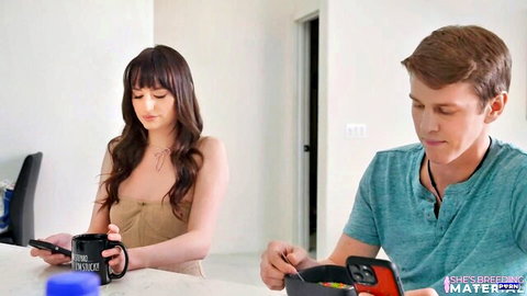 Petite brunette teen with small tits cleavage holds SHE'S YOUR mug and phone next to stepbrother in kitchen