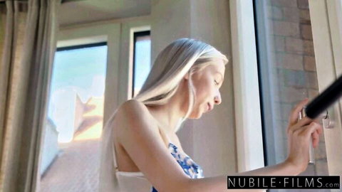 Blonde babe in sheer blue lingerie teasing her perky tits by sunlit window