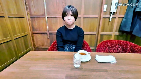 Petite Japanese girl in black top and plaid skirt sits at wooden table with tea cup