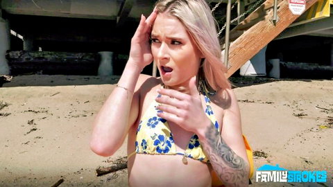 Shocked blonde with tattoos grabs her floral bikini top on sunny beach