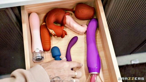 Drawer overflowing with colorful dildos and vibrators, tattooed hand grabbing thick purple cock toy