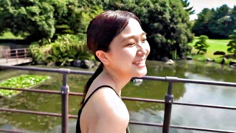 Smiling Asian woman in black tank top posing by scenic Japanese garden pond