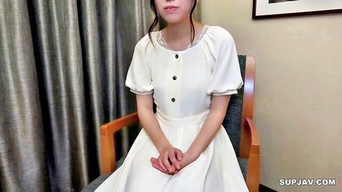 Cute Asian student babe in white lace dress sitting demurely on chair with hands in lap