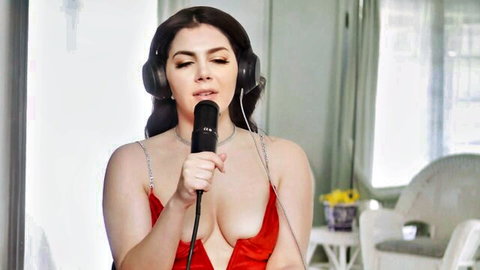 Busty brunette with massive tits and deep cleavage sings into mic in skimpy red dress