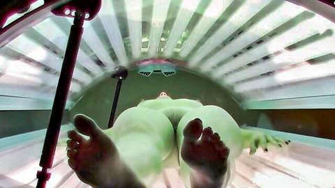 Nude student in solarium tanning bed, feet soles close-up
