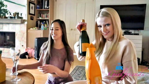 Blonde and brunette girlfriends smiling while toasting champagne in cozy living room sweaters