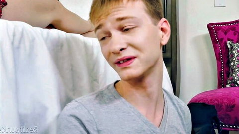 Freckled blond twink squints with open mouth as woman's hand grips his face in bedroom