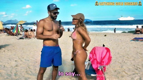 Busty blonde Latina in skimpy pink thong bikini flaunts big ass and tits during beach interview with shirtless hunk