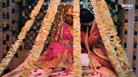 Desi bride and groom in traditional wedding attire on floral bed