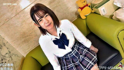 Cute Japanese schoolgirl in sailor uniform smiles teasingly on couch with teddy bear