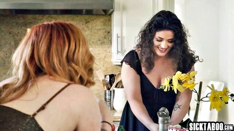 Curvy brunette MILF with huge breasts in black dress and redhead friend in kitchen