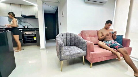 Topless Latina woman cooking in kitchen, shirtless hunk on couch in amateur home setup