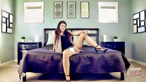 Sexy brunette babe spreading legs on bed in heels and short shorts