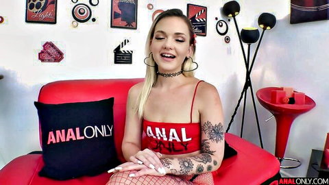 Smiling blonde in red fishnet lingerie posing seductively on red couch with analonly pillow