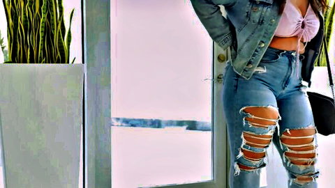 Curvy brunette in ripped jeans and pink crop top posing seductively