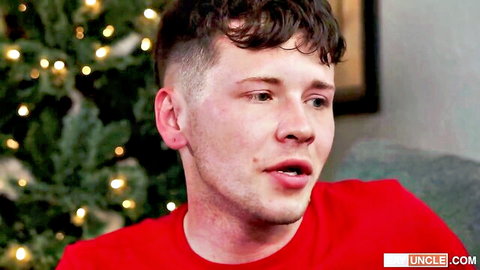 Young pale twink in red shirt smirks by Christmas tree in gay taboo video