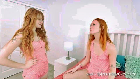 Two sexy redhead babes in tight pink rompers teasing on bedroom bed