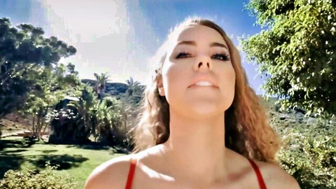 Sexy tanned blonde in tight red tank top smiling seductively outdoors in sunny park