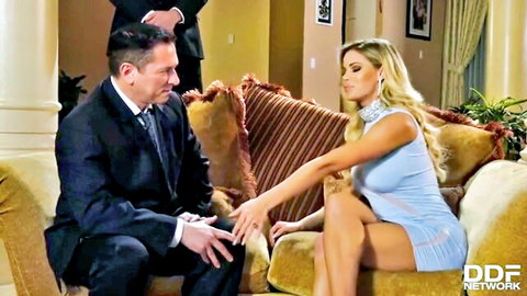 Blonde bombshell in tight blue mini dress flirts intimately with suited man on couch while another watches