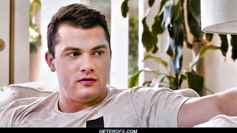 Young handsome brunette guy lounging on couch in tight gray t-shirt looking seductive