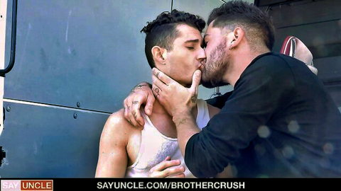 Two muscular tattooed gay hunks passionately kissing and grabbing intensely against metal wall