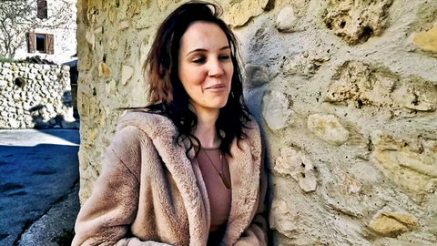 Cataleya, 28, in open fur coat showing cleavage against wall