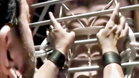 Submissive Chet Walker gripped in BDSM cage with leather cuffs, dom in control
