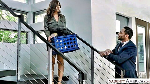 Curvy olive-skinned brunette in short skirt holds blue crate on stairs as suited man gazes up hungrily