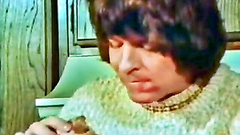Vintage shaggy-haired brunette in sweater gazes down at hand gripping small object seductively