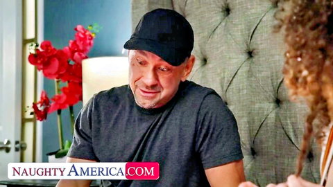 Smiling DILF stepdad in black cap eyes young curly-haired beauty on Naughty America bed