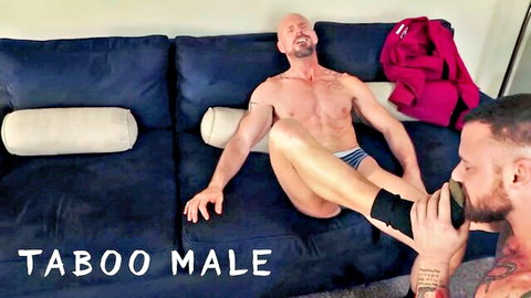 Muscular bald guy in briefs lounges as bearded bro trims his leg in taboo gay scene