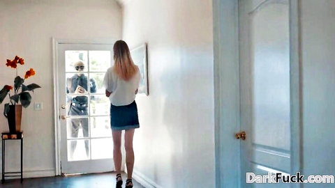 Blonde teen in tiny denim skirt stands at glass door as suited man spies on her