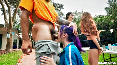 Purple-haired babe kneels sucking massive black cock outdoors at party with redhead watching