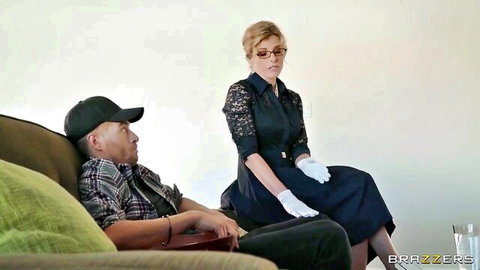 Blonde woman in lace dress white gloves and glasses stands seductively over lounging man on couch